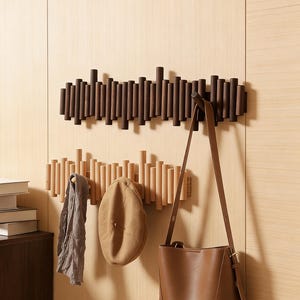 May include: Two wooden coat racks with vertical dowels mounted on a light wood wall. The top rack is dark brown, and the bottom rack is natural wood. A brown leather purse, a gray scarf, and a tan hat hang from the racks.