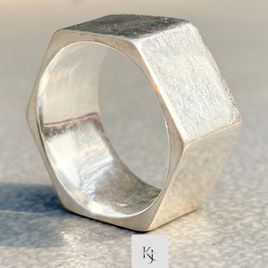 May include: A silver ring with a hexagonal design. The ring has a solid appearance and a smooth, polished surface. The ring is a piece of jewellery, suitable for everyday wear. The ring's design is geometric.