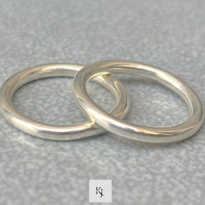 Puede incluir: Dos anillos de plata entrelazados, sobre un fondo gris texturizado. Los anillos son lisos y circulares, reflejando la luz. Los anillos parecen ser de un metal brillante, posiblemente plata de ley.