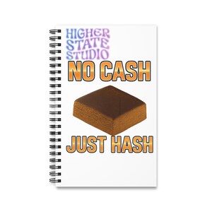 Op de afbeelding: Een witte spiraalgebonden notitieboek met de tekst "HIGHER STATE STUDIO" in een verlooplettertype. De woorden "NO CASH" en "JUST HASH" staan in oranje blokletters. Een bruin, rechthoekig object is gecentreerd op het notitieboek.