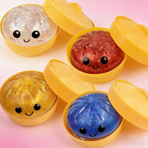 May include: Four colourful, glittery dumpling-shaped toys with smiling faces. Each dumpling is in a yellow container with a lid. The dumplings are silver, red, gold, and blue. The toys are designed to look like steamed buns.