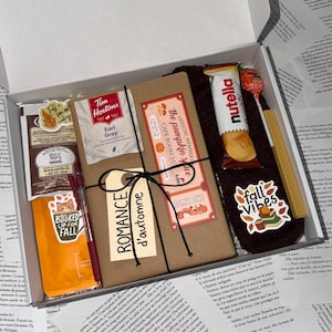 May include: A gift box containing a book wrapped in brown paper with a black string, a Tim Hortons Earl Grey tea bag, a Nutella B-ready snack bar, a lollipop, a red pen, a yellow highlighter, a pair of dark brown socks, and three fall-themed stickers.