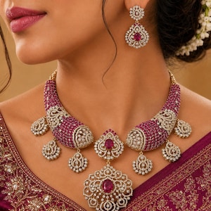 May include: A jewelry set consisting of a necklace and matching drop earrings. The necklace features a curved, wide band encrusted with small magenta stones and clear crystals, with dangling filigree pendants and a large central oval magenta stone.