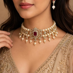 May include: A gold-toned choker necklace featuring rows of cream-colored pearls, intricate filigree metalwork, and a central rectangular deep red gemstone. Matching drop earrings feature a similar red gemstone and a single dangling pearl.