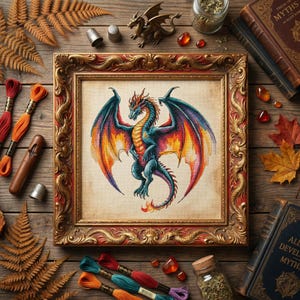 Puede incluir: Obra de arte de punto de cruz de un dragón con alas azules, naranjas y moradas, enmarcada en un marco dorado ornamentado. El dragón está centrado sobre un fondo crema. Hilos de bordar, dedales y una pequeña figura de dragón rodean la obra enmarcada.