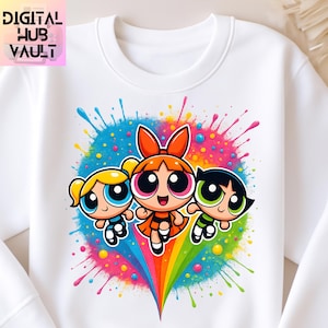 Puede incluir: Sudadera blanca de cuello redondo con un gráfico colorido de tres personajes de dibujos animados. El diseño incluye un arcoíris y un efecto de salpicaduras de pintura. El texto "DIGITAL HUB VAULT" está en la esquina superior izquierda.