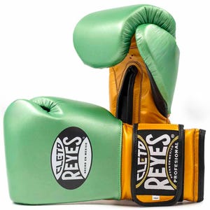 Peut inclure: Une paire de gants de boxe Cleto Reyes de 14oz avec une finition vert métallisé sur les articulations et le pouce, contrastée par un poignet et une paume dorés. L'écusson ovale noir affiche le texte Cleto Reyes Hecho en Mexico.