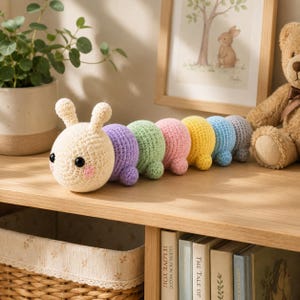 Peut inclure: Un jouet chenille au crochet composé d'une tête crème avec des yeux noirs et des joues roses, suivi d'un corps segmenté en violet, vert clair, rose, jaune, bleu et gris. Le jouet possède deux petites antennes sur le dessus de sa tête ronde.