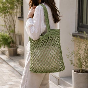 Woman carrying handmade sage green crochet mesh tote bag outdoors with neutral outfit, realistic size reference, elegant lifestyle fashion product photography.