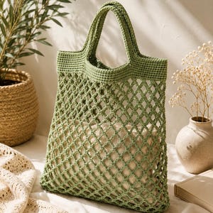 Handmade sage green crochet mesh tote bag hanging on wooden chair in cozy minimalist interior with warm sunlight and natural home decor styling.