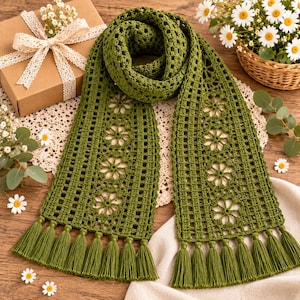 May include: An olive green crochet scarf featuring a repeating floral motif pattern, a grid-like texture, and long fringe tassels at both ends. The scarf is crafted with a detailed openwork stitch design, showcasing a consistent color and style.