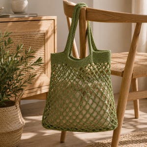 Puede incluir: Una bolsa de red verde tejida a ganchillo cuelga de una silla de madera. La bolsa tiene forma rectangular con un dise&ntilde;o de red tejida y asas resistentes. La bolsa est&aacute; llena de tela de color claro, ideal para ir de compras.