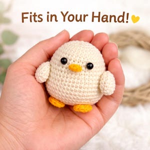 May include: A crocheted chick with a cream-colored body, black eyes, and an orange beak and feet. The text "Fits in Your Hand!" is above the chick. The chick is held in a hand.