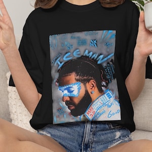 Puede incluir: Una camiseta negra con un estampado gr&aacute;fico de un hombre con barba, estilizado con acentos de aer&oacute;grafo azul sobre los ojos y el texto "ICEMAN" sobre la cabeza. El texto adicional incluye "MAY 15", "Papi" y "6GOD" en letras azules y rojas.