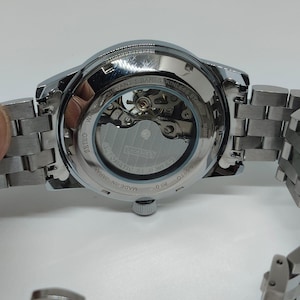 May include: A silver Seiko automatic wristwatch with a stainless steel strap. The watch has a transparent back, revealing the internal mechanism. The watch is marked "Made in Japan" and "Water Resistant 5 Bar".