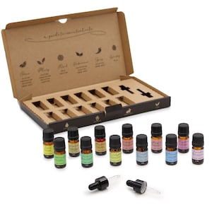May include: A collection of essential oils in small amber glass bottles with black lids, presented in a cardboard box. The box is open, showing individual compartments for each bottle. The labels on the bottles are colourful, and two droppers are in front.