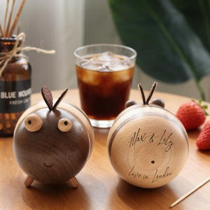 Könnte beinhalten: Zwei bienenförmige Holzfiguren. Eine ist dunkelbraun mit hellbraunen Streifen und Holzbeinen. Die andere ist hellbraun mit dunkelbraunen Streifen und der Aufschrift "Max & Lily Love in London".