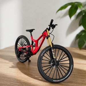 Könnte beinhalten: Ein Miniatur-Mountainbike in Rot mit schwarzen Reifen und einem schwarzen Sattel. Das Fahrrad hat goldfarbene Federgabeln und einen schwarzen Lenker. Das Fahrrad ist ein detailliertes Modell, das das Design eines vollgefederten Mountainbikes zeigt.
