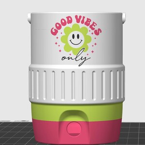 May include: A white cylindrical beverage cooler featuring a graphic of a light green flower with a smiley face, surrounded by pink stars and the text "GOOD VIBES only". The cooler has a ribbed white middle section and a lime green and pink base.