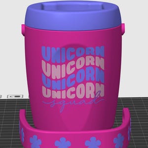 May include: A bright pink cylindrical container with a purple lid and a matching pink handle featuring purple flower accents. The front displays the text UNICORN stacked four times in alternating purple and light pink, followed by the word squad.