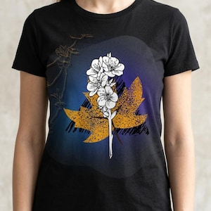 May include: Black t-shirt with a graphic of white flowers on a stem, set against a yellow leaf and a blue and purple gradient background. The design has a vintage, slightly distressed appearance.