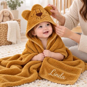 May include: A mustard yellow hooded towel featuring a bear face design on the hood with embroidered ears and a dark brown nose. The towel is made of soft, textured fabric and includes the name Linda embroidered in white script on the corner.