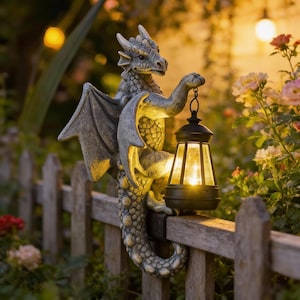 Puede incluir: Una estatua de dragón gris con alas extendidas sosteniendo una linterna negra en una valla de madera. La linterna emite una luz cálida. La escena se desarrolla al aire libre, con flores en el fondo.