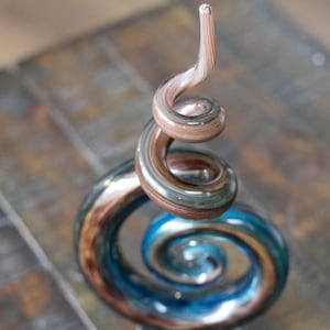May include: A decorative glass sculpture with a spiral design. The sculpture features a combination of brown, blue, and clear glass, creating a visually appealing piece. The spiral shape adds a dynamic element to the artwork.
