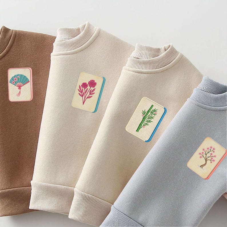 Puede incluir: Cuatro sudaderas de cuello redondo en marr&oacute;n, crema, beige y azul claro. Cada sudadera presenta un parche rectangular en el pecho que representa una ficha de mahjong con ilustraciones de un abanico, flores, bamb&uacute; y un &aacute;rbol.