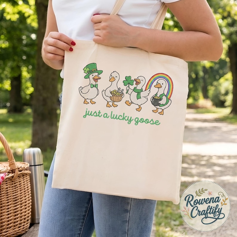 May include: Cream-colored tote bag featuring a whimsical design of cartoon geese celebrating St. Patrick's Day. The geese are adorned with festive accessories like a green hat, shamrock, and pot of gold. The text "just a lucky goose" is printed in green.