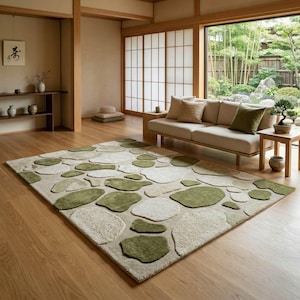 May include: A beige area rug with a stone pattern in shades of green and off-white. The rug is in a living room with a wooden floor, a light-colored sofa, and a large window overlooking a garden.