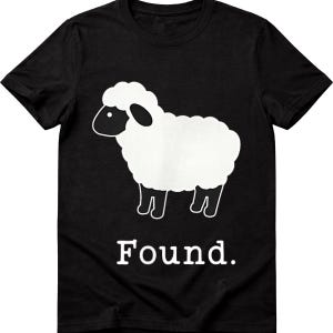 May include: A black short-sleeved t-shirt featuring a graphic of a white sheep with a black head and legs. Below the sheep, the word "Found." is printed in a white serif font. The design is centered on the front of the garment.