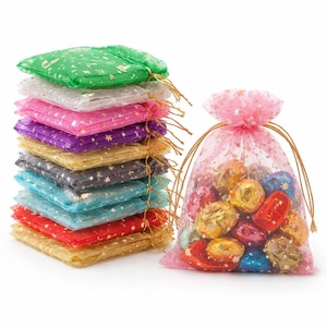 Op de afbeelding: Een stapel kleurrijke, doorschijnende cadeauzakjes met gouden sterpatronen en trekkoordsluitingen. Naast de stapel staat een roze zakje gevuld met verpakte snoepjes. De zakjes zijn in verschillende kleuren, waaronder groen, wit, roze en rood.