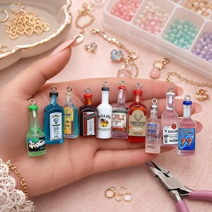 Könnte beinhalten: Eine Sammlung von zehn Miniatur-Flaschenanhängern mit verschiedenen Spirituosen-Etiketten wie Bombay Sapphire, Malibu, Old Captain, Absolut Vodka und Bacardi. Jede kleine Glasflasche ist mit einer silberfarbenen Metallöse zum Aufhängen versehen.