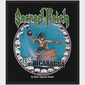 Puede incluir: Un parche rectangular negro con el texto verde Sacred Reich en la parte superior. Un marco circular contiene una figura de dibujos animados surfeando sobre un ataúd mientras sostiene una bomba. El texto Surf Nicaragua aparece debajo, rodeado de calaveras.