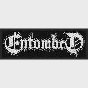 May include: A rectangular black fabric patch featuring the word Entombed embroidered in white thread. The lettering is rendered in a stylized, jagged, gothic-inspired font with a textured appearance, set against a solid black background.