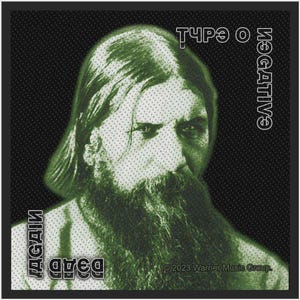 Op de afbeelding: Een vierkante patch met een groen halftoonportret van een bebaarde man. De tekst "TYPE O NEGATIVE" staat rechtsboven, terwijl "DEAD AGAIN" linksonder is gedrukt. Het copyright "© 2023 Warner Music Group" staat onderaan.
