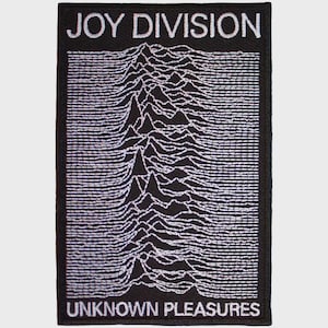 May include: A rectangular black embroidered patch featuring the white text JOY DIVISION at the top and UNKNOWN PLEASURES at the bottom. The centre displays a white graphic of radio waves or mountain-like peaks against a solid black background.