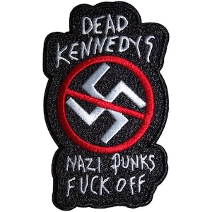 May include: A black embroidered patch featuring the white text DEAD KENNEDYS at the top and NAZI PUNKS FUCK OFF at the bottom. In the centre, a white swastika is depicted inside a red circle with a red diagonal line crossing through it.