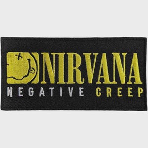 May include: A rectangular black embroidered patch featuring a yellow Nirvana logo with a stylized smiley face icon on the left side. Below the band name, the text NEGATIVE CREEP is embroidered in white capital letters on the black fabric background.