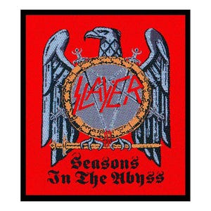 Peut inclure: Écusson brodé avec un aigle gris aux ailes déployées, un emblème circulaire avec le mot "SLAYER" en rouge et le texte "Seasons In The Abyss" sur fond rouge. L'écusson a une bordure noire.