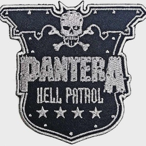 Puede incluir: Un parche bordado en forma de escudo en blanco y negro. El diseño presenta una calavera con tibias cruzadas en la parte superior, el texto PANTERA en letras grandes, el texto HELL PATROL debajo y una fila de cuatro estrellas con borde blanco.