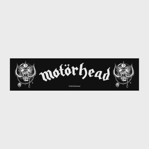 Peut inclure: Un écusson rectangulaire en tissu noir présentant le texte blanc "motörhead" dans une police gothique stylisée. Le motif comprend une illustration blanche détaillée d'une créature à crâne cornu et à défenses de chaque côté du texte.