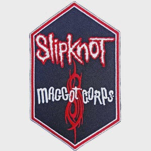 Könnte beinhalten: Ein sechseckiger gestickter Aufnäher mit dunkelblauem Hintergrund und rotem Rand. Der Schriftzug Slipknot ist in Weiß mit roter Umrandung gestickt, der Schriftzug Maggot Corps ist in Weiß gehalten. Ein rotes Nonagramm-Symbol ist unter dem Text zentriert.