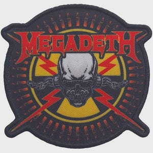 May include: A circular embroidered patch featuring the red text MEGADETH across the top. The center displays a white skull with black shading, wearing dark sunglasses, set against a yellow radiation symbol and red lightning bolts on black.