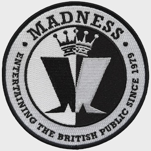 May include: A circular embroidered patch featuring a black and white split design. The text MADNESS is at the top, and ENTERTAINING THE BRITISH PUBLIC SINCE 1979 is at the bottom. A central crown sits above two stylized letter W shapes.