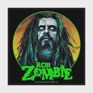 Könnte beinhalten: Ein quadratischer Aufnäher mit einer kreisförmigen Grafik von Rob Zombie mit langem dunklem Haar, Bart und genähten Gesichtsmarkierungen. Das Bild verwendet Grün-, Gelb- und Schwarztöne. Der Text ROB ZOMBIE erscheint in hellem Grün unter dem Porträt.