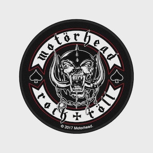 Op de afbeelding: Een ronde zwart-witte geborduurde patch met de Motörhead Snaggletooth-mascotte met hoorns en kettingen. De tekst luidt Motörhead en rock 'n' roll met schoppensymbolen aan de zijkanten en een klein kruisje aan de onderkant. © 2017 Motorhead.