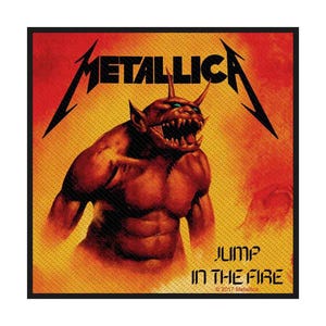 Puede incluir: Un parche cuadrado con el logo de Metallica y una figura demoníaca roja con cuernos y dientes afilados. El texto "JUMP IN THE FIRE" está debajo de la ilustración, sobre un fondo naranja y amarillo llameante.
