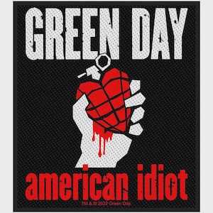 May include: A rectangular patch featuring the text GREEN DAY in white at the top and american idiot in red at the bottom. The center displays a white hand holding a red heart-shaped grenade with black grid lines and red liquid dripping downward.